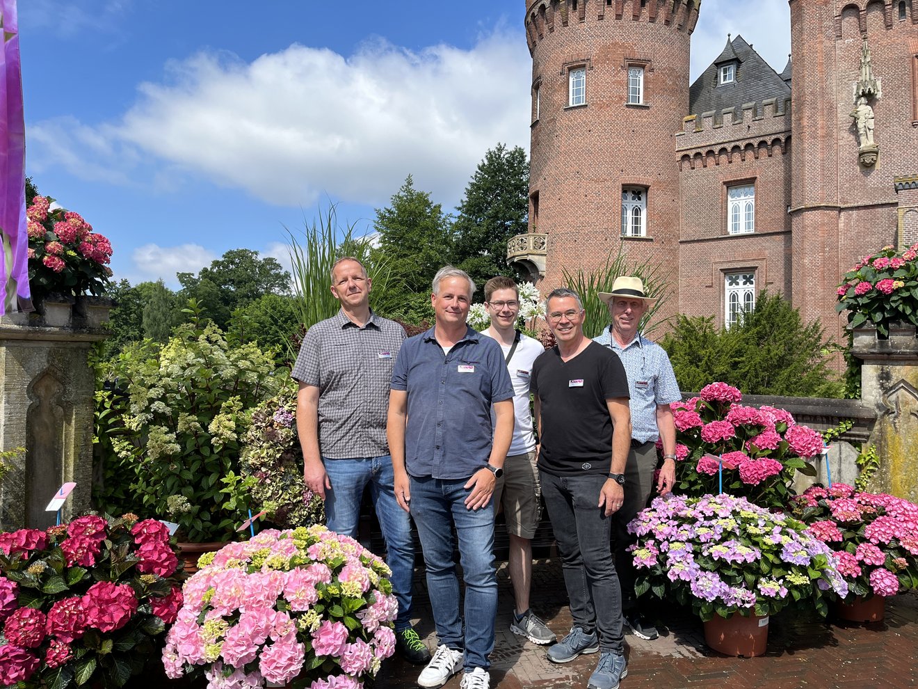 Personen vor schloss mit verschiedenfarbigen Hortensien