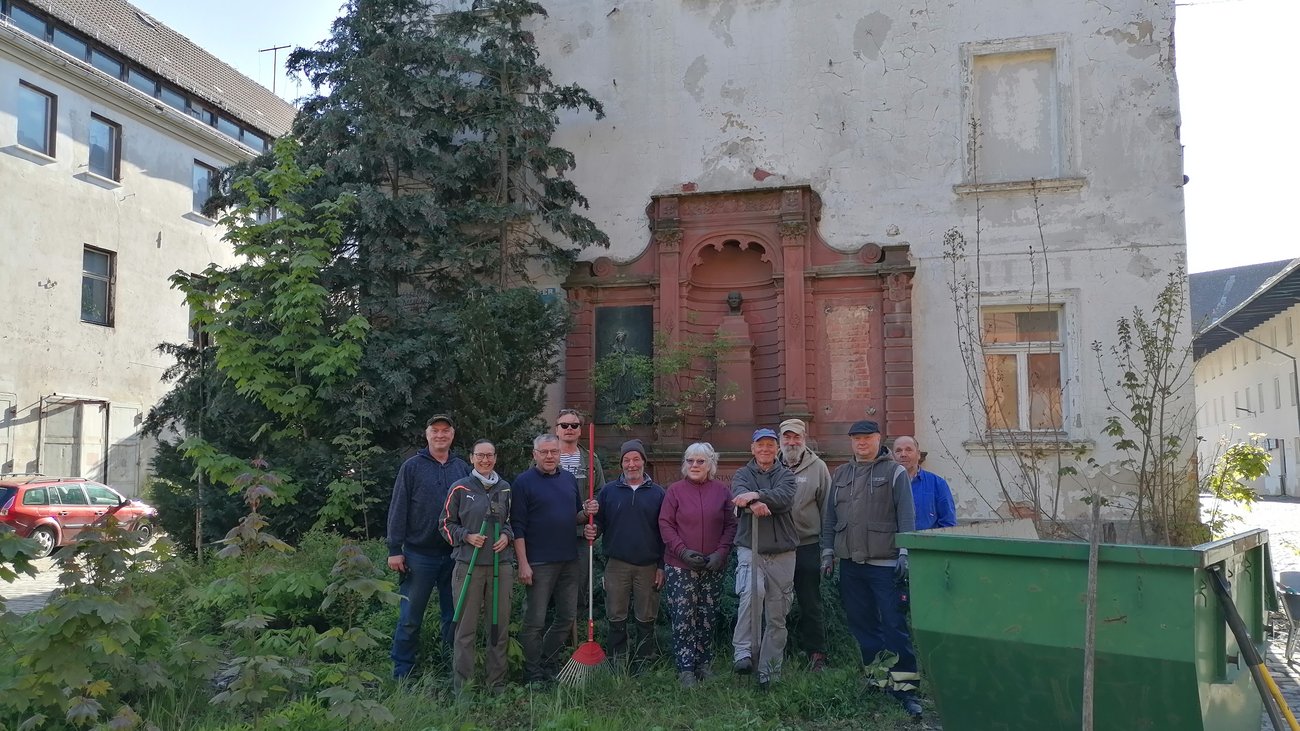 Menschengruppe mit Werkzeug auf der Wiese  vor Haus
