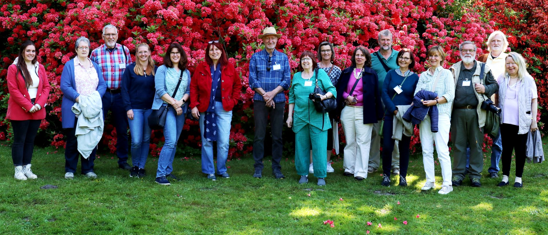Menschengruppe vor rotbl&uuml;hendem Rododendron